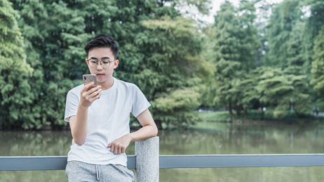 男青年依靠在公园栏杆旁看手机