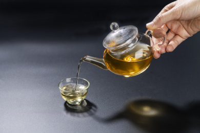 手持仿古玻璃茶壶向玻璃茶杯中倒茶黑色背景
