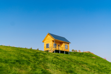 晴朗蓝天下乡村山坡草地上的黄色小房子