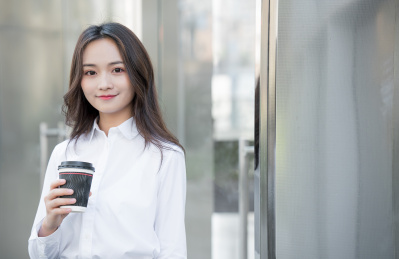 年轻商务女性手拿咖啡杯在办公室外休息