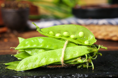 黑底上放着一捆青豆荚和一个剥开的豌豆荚