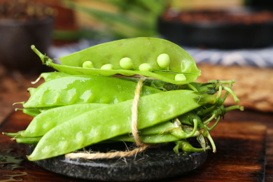 黑底上放着一捆青豆荚和一个剥开的豌豆荚