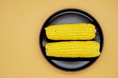 橙色背景中放在黑色盘子里的两根甜玉米