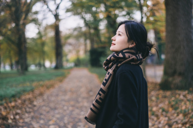 穿黑色大衣和围巾的女孩，在深秋落叶森林里