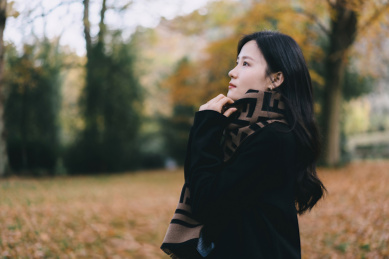 穿黑色大衣和围巾的女孩，在深秋落叶森林里