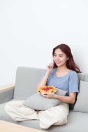 女孩坐在沙发上边吃水果边看电视