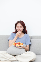 女孩坐在沙发上边吃水果边看电视