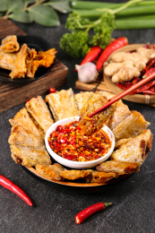 黑底上放着一盘秘制酥带鱼和筷子上夹着带鱼