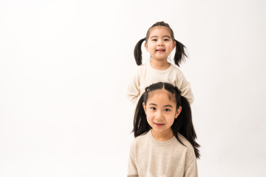 两名坐在白色背景前玩耍的姐妹