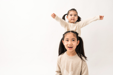 两名坐在白色背景前玩耍的姐妹