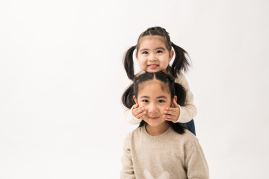 两名坐在白色背景前玩耍的姐妹