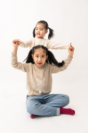 两名坐在白色背景前玩耍的姐妹