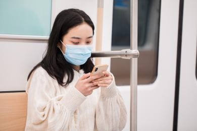 戴着口罩坐地铁玩手机的年轻女性