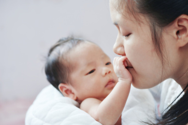 年轻妈妈亲吻婴儿的小手