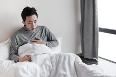 男子坐在床上用手捂住胸口