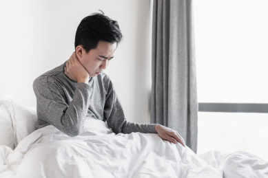 年轻男子坐在床上用手捂住脖子