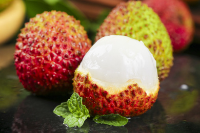 黑底上放着两颗完整的荔枝和一颗剥开皮丹荔