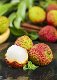 黑底上放着两颗完整的荔枝和一颗剥开皮丹荔