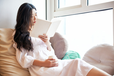 躺在舒适的飘窗上喝水看书的准妈妈