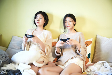 在客厅沙发床上打游戏的两位亚洲年轻女性