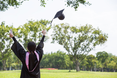 毕业季校园里穿着学士服的女孩扔帽子背影