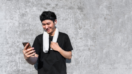 运动男子靠墙笑着使用手机