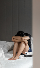 沮丧的男子坐在床上埋头抱住膝盖