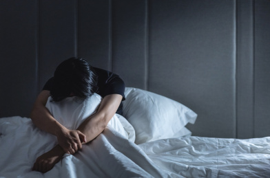 沮丧的男子坐在床上埋头抱住膝盖