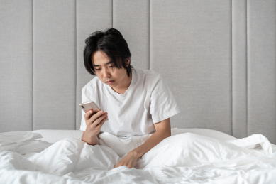 坐在床上头发凌乱的男子正在看手机