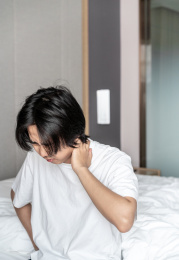 年轻男子坐在床边皱眉捂着脖子
