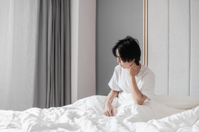 年轻男子坐在床上用手捂住脖子