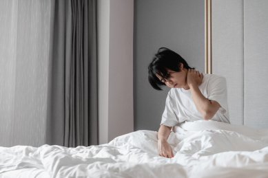 年轻男子坐在床上用手捂住脖子