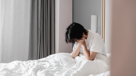 年轻男子坐在床上低头双手捂脸