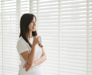 女生站在窗边手拿杯子看向窗外