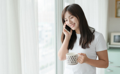 美女站在窗边使用手机打电话