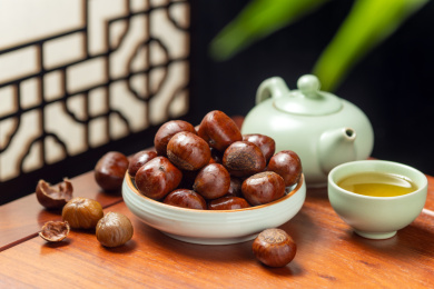 一盘糖炒栗子摆放在古窗棂背景木桌面上