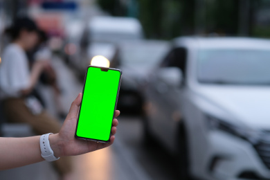 手在车流前展示绿屏的手机