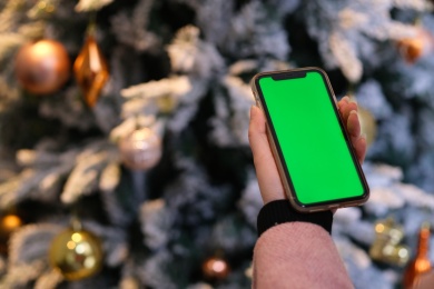 圣诞树前手拿着绿屏的手机