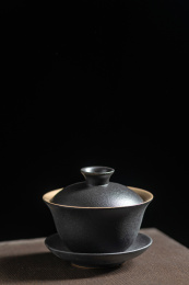 黑陶茶具三才杯盖碗与铁壶摆放在木桌面上