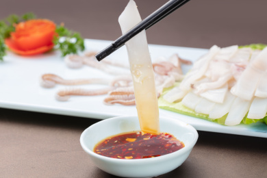 白盘里的筷子夹着蘸料的生吃鱿鱼