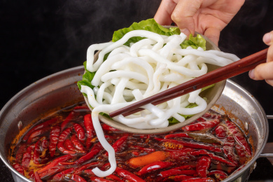 筷子夹着正在沸腾老火锅汤里烫火锅土豆粉