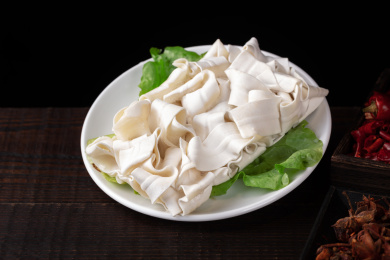 深色桌上白盘里的重庆老火锅菜品宽面条