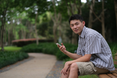 年轻帅气的中国男子在户外公园使用手机
