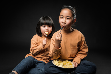坐在黑背景前吃水果的两个亚裔女孩