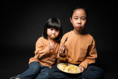 坐在黑背景前吃水果的两个亚裔女孩