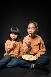 坐在黑背景前吃水果的两个亚裔女孩