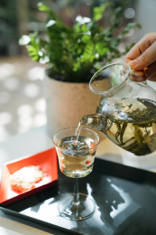 在阳光下手拿玻璃茶壶把茶水倒入茶杯中