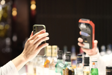 在有很多酒瓶的酒吧里手拿手机扫码支付付款