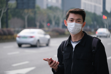 街头戴着口罩的年轻中国男子拿着手机
