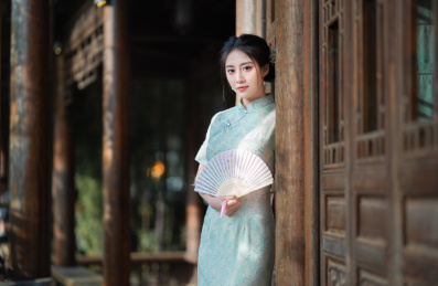 穿旗袍的女子拿着扇子站在门前